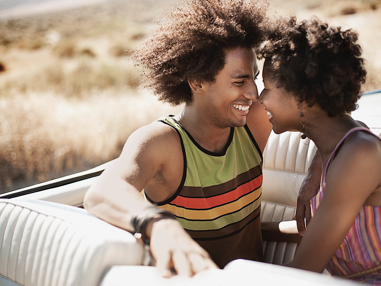 A young couple, man and woman in a pale blue convertible, n the back seat close together laughing. by Mint_Images
